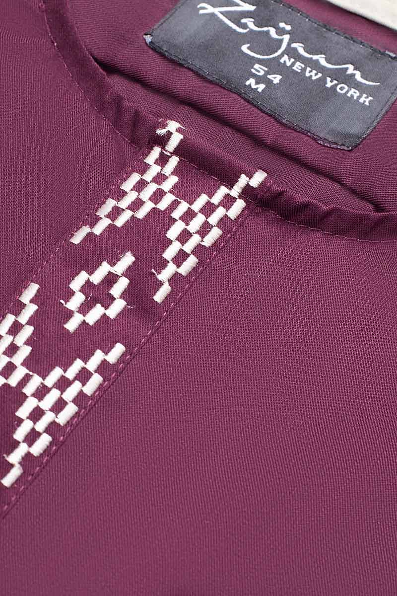 Close-up of white geometric embroidery on the maroon fabric of an Emirati thobe