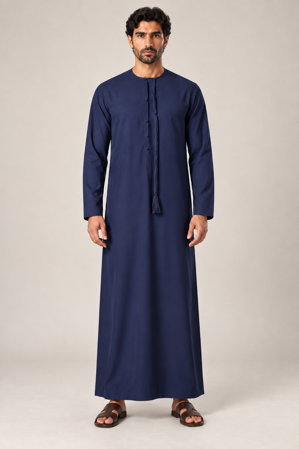 Male model wearing a navy blue Emirati thobe with long sleeves and decorative tassel neckline, full front view
